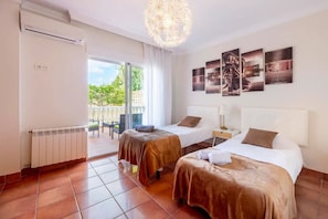 A hotel room with two beds, a radiator, a ceiling light, and a view of the outdoors.