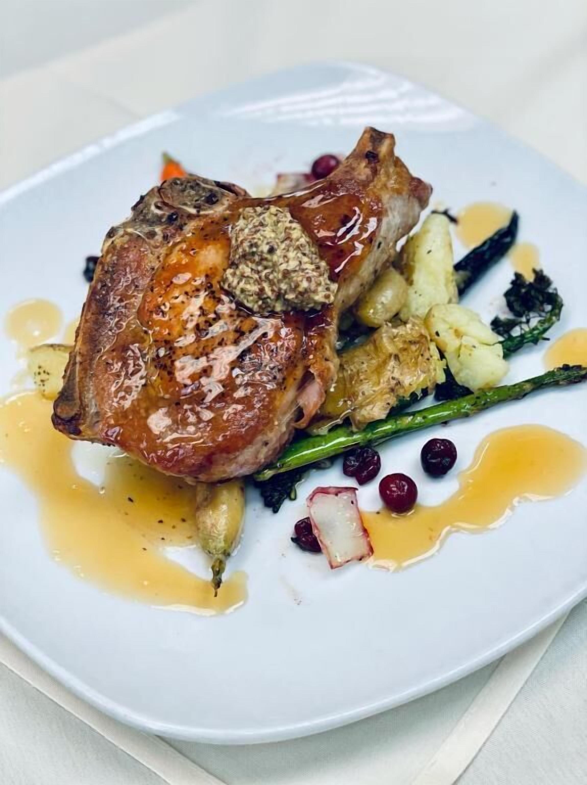 A plate with a roasted pork chop, asparagus, and a sauce.