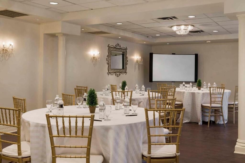 A conference room with round tables, chairs, and a projector screen.