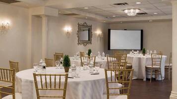 A conference room with round tables, chairs, and a projector screen.