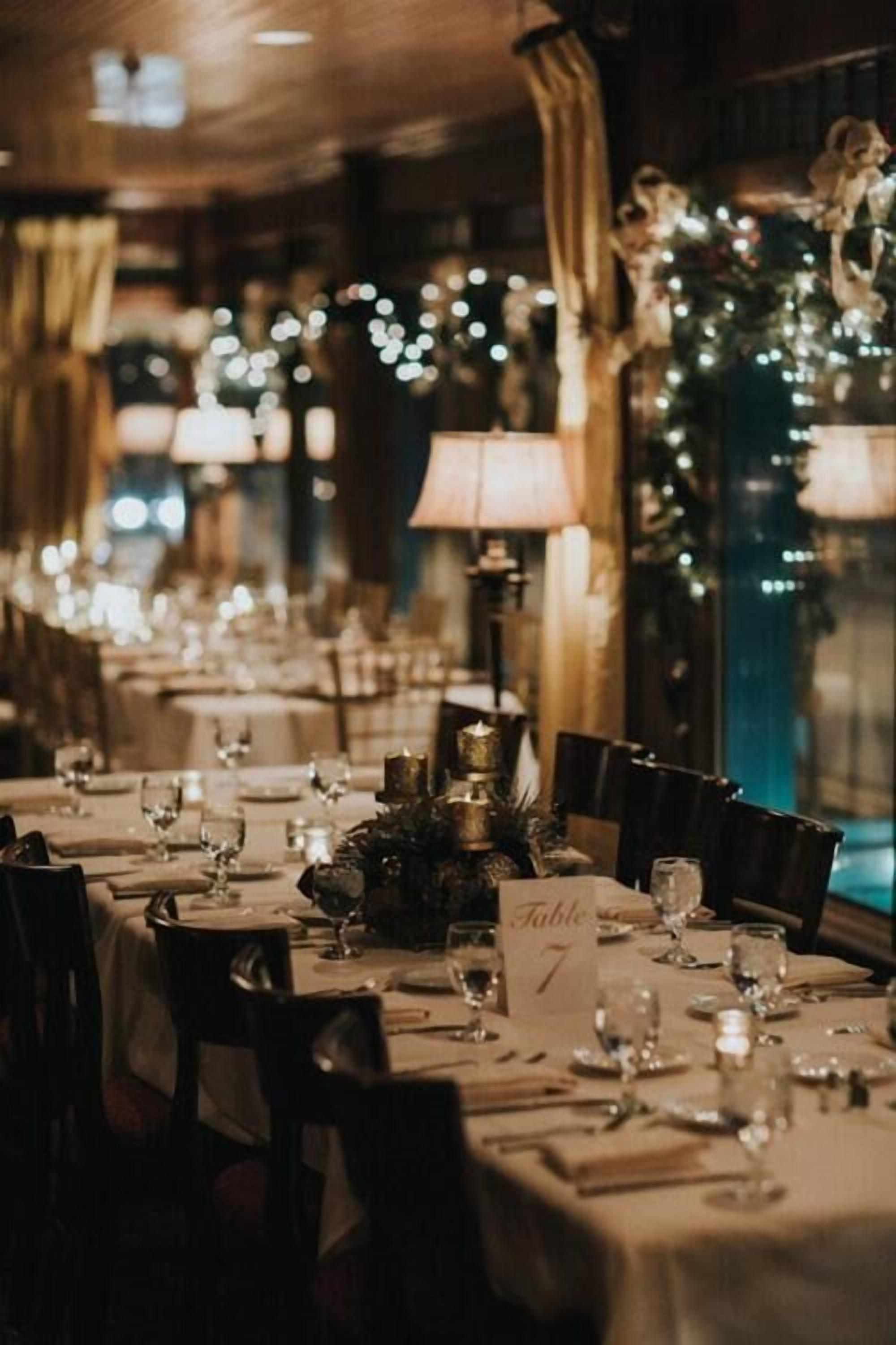 Un restaurant où les tables sont dressées pour le dîner, chacune étant agrémentée d’une bougie et d’un menu.