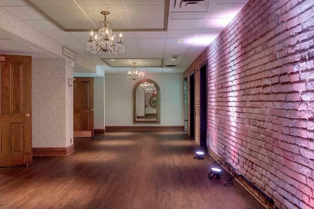 A hallway with wooden flooring, a brick wall on one side, and a chandelier.
