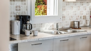 Eine Küche mit Fenster, einer Kaffeemaschine, einem Wasserkocher, einer Spüle und einer Reibe.