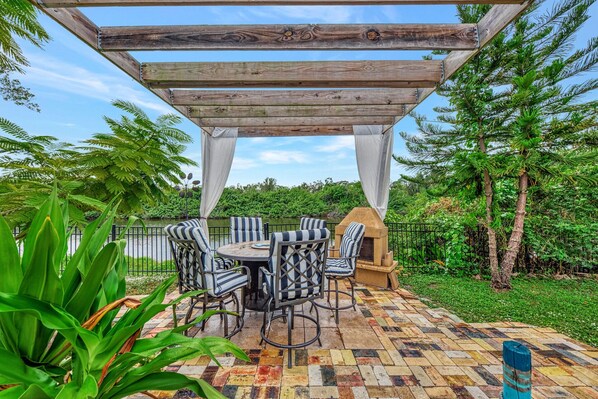 Un patio exterior con una pérgola de madera, sillas a rayas y una mesa redonda.