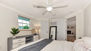 A bedroom with a bed, a dresser, a ceiling fan, a window, and a door leading to a bathroom. - My Venice Beach House (South Venice)