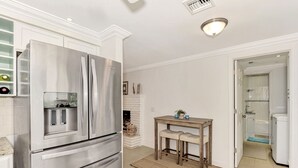 A modern kitchen with a stainless steel refrigerator, a wooden table with two chairs, and a white tiled floor. - My Venice Beach House (South Venice)