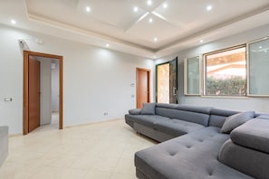 A modern living room with a sectional sofa, a glass door leading to a balcony, and a tiled floor. - Villa 'Villino Giovanna' with Private Terrace, Wi-Fi and Air Conditioning (Trabia)