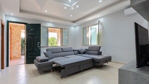 A modern living room with a sectional sofa, a flat-screen TV, and a large window. - Villa 'Villino Giovanna' with Private Terrace, Wi-Fi and Air Conditioning (Trabia)