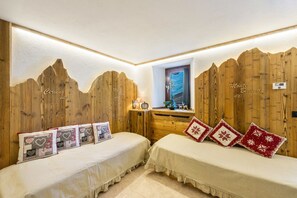A room with two beds, wooden panel walls, a window with a view, and a small table with a clock and decorative items.