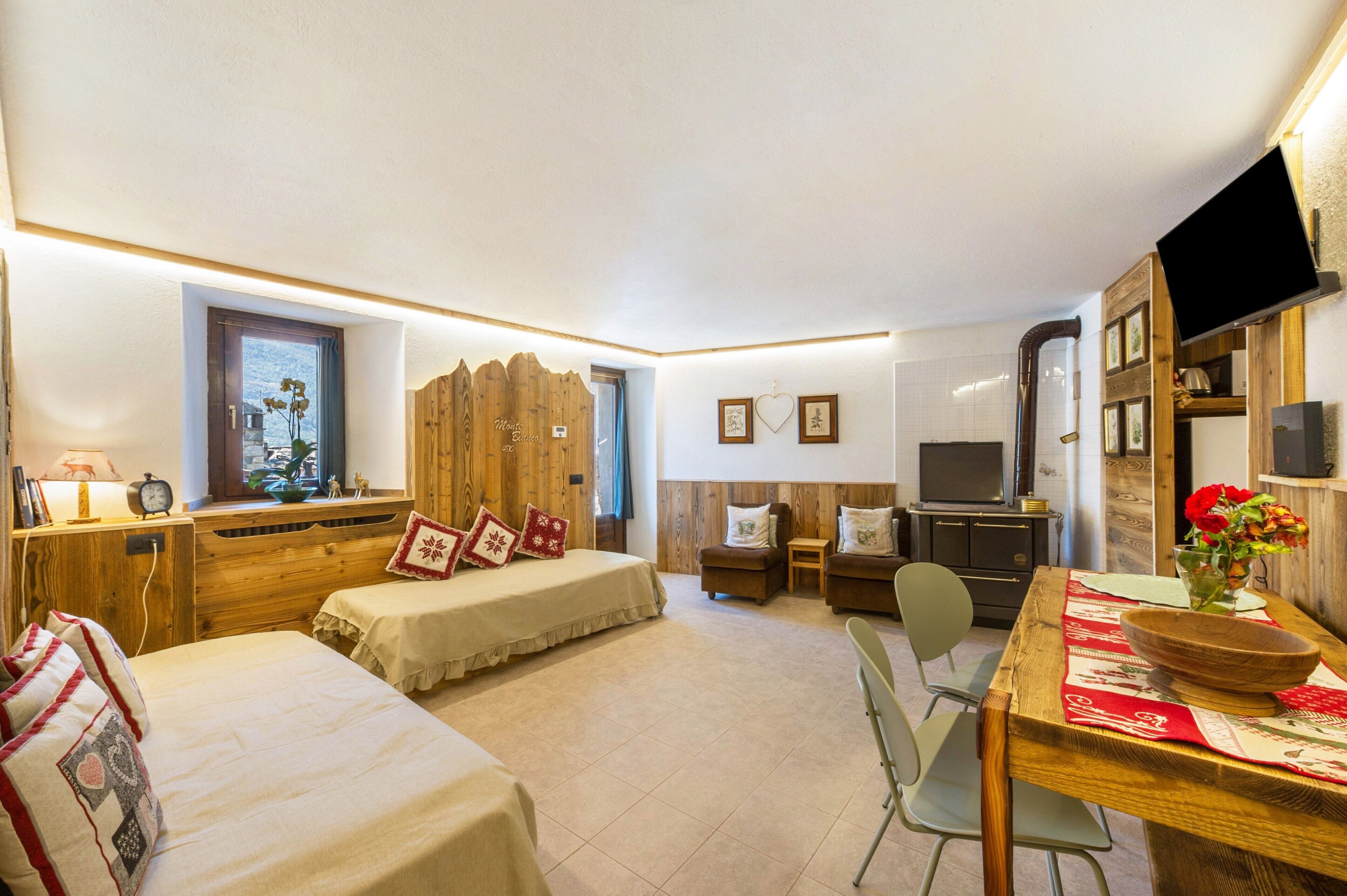 A room with two beds, a TV, a wooden dining table, and a window with a view.