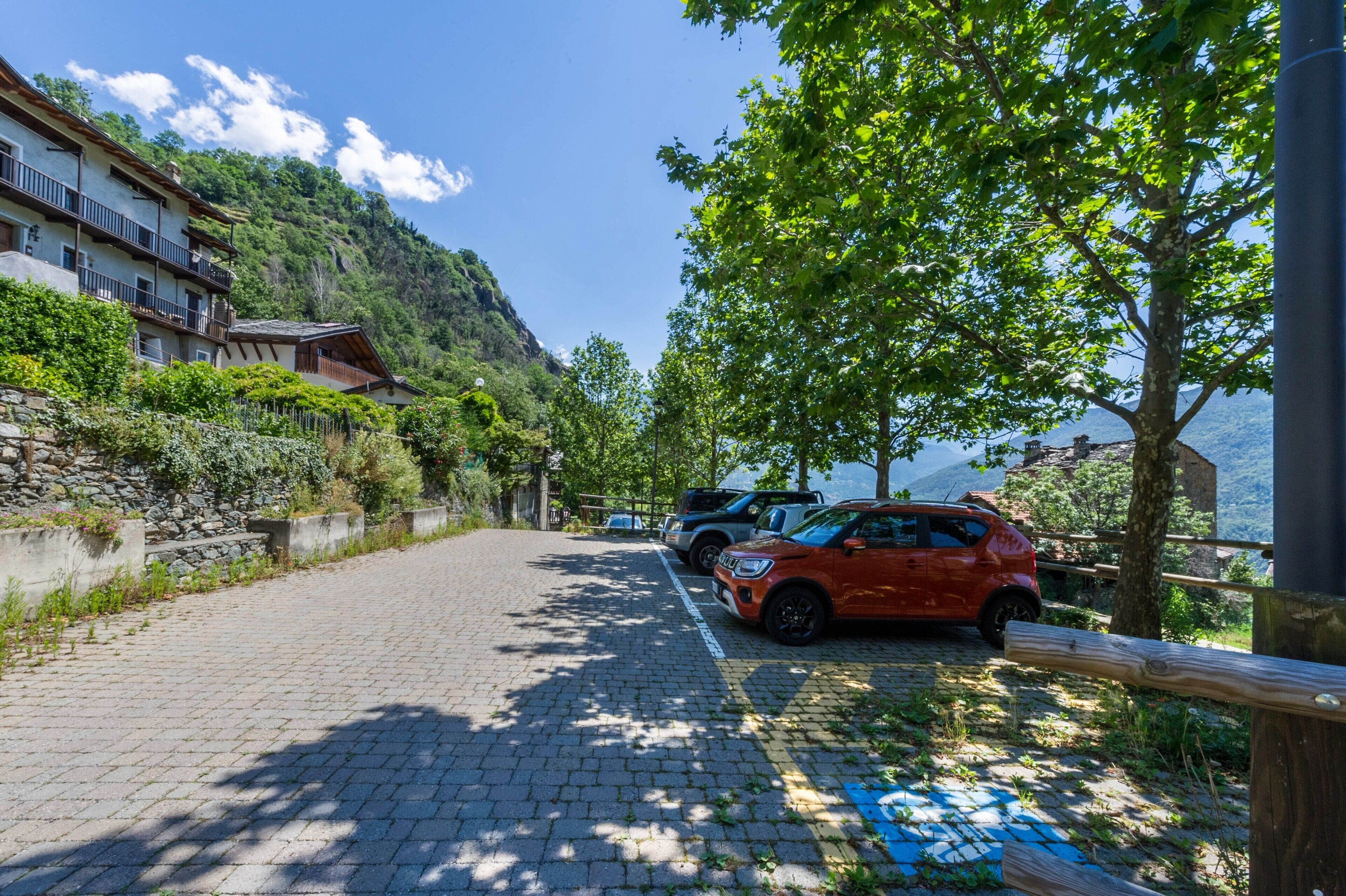Un chemin pavé bordé de voitures garées, un immeuble doté de balcons et une montagne en arrière-plan.