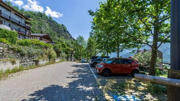Un chemin pavé bordé de voitures garées, un immeuble doté de balcons et une montagne en arrière-plan.