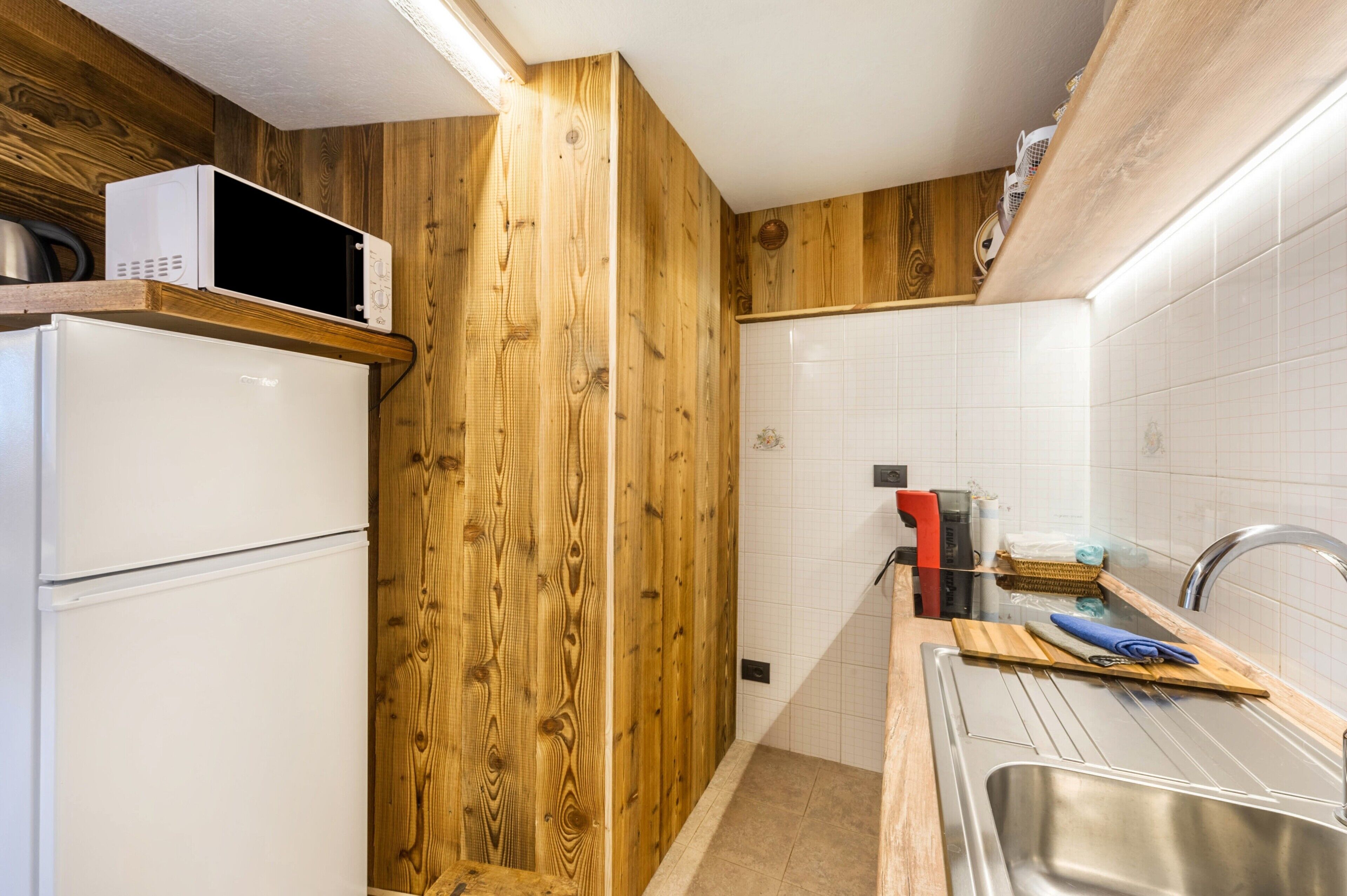 Eine Küche mit Holzwänden, einem weißen Kühlschrank, einer Mikrowelle und einem Spülbecken mit Schneidebrett und Messer.