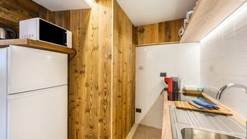 Eine Küche mit Holzwänden, einem weißen Kühlschrank, einer Mikrowelle und einem Spülbecken mit Schneidebrett und Messer.