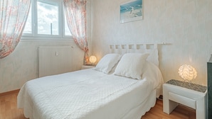 Une chambre à coucher avec un lit, des rideaux, une table de chevet, une lampe et un tableau au mur.