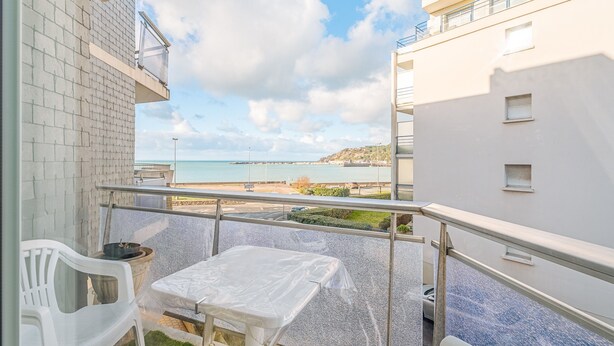 Un balcon avec une table et des chaises, une vue sur la mer et un immeuble à la façade blanche.