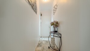 Un couloir avec un sol à motifs, une porte au fond et une petite table sur laquelle est posé un vase de fleurs.