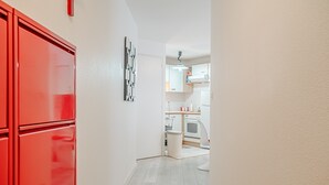 A hallway with a red cabinet, a white wall, and a kitchen area in the background.