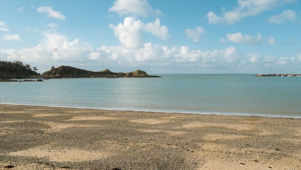 A beach with pebbles, calm water, and distant islands.