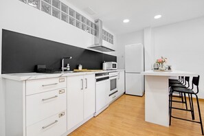 A modern kitchen with white cabinetry, a black backsplash, a stainless steel range hood, a microwave, and a small island with bar stools. - Vacation Apartment 'Ca L'Oliera' with Balcony, Wi-Fi, and Air Conditioning (Denia)