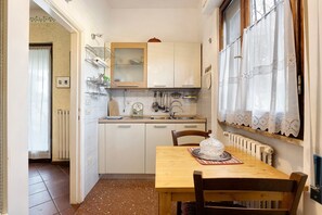 A compact kitchen with white cabinets, a wooden table, and a window with lace curtains.