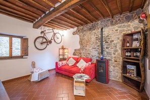 A cozy room with a red sofa, a stone wall, a wooden ceiling, a bicycle, a fireplace, and a wine rack. - Holiday Home 'L'arco Della Fonte' with Private Terrace, Wi-Fi and Air Conditioning (Gaiole in Chianti)