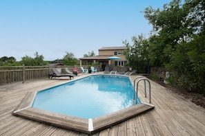 Une terrasse en bois avec une piscine, des chaises longues et une maison en arrière-plan.
