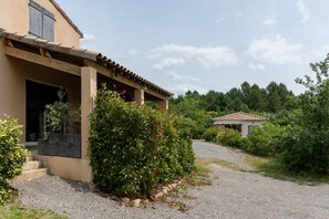 Una casa con un portico coperto, un vialetto sterrato e un piccolo edificio sullo sfondo.