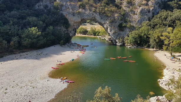 A river with kayaks lined up on the shore, a rocky arch formation, and a beach. - Holiday Home 'Le Pequelet' with Shared Pool, Wi-Fi and Air Conditioning (Payzac)