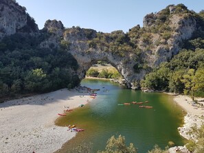 A river with kayaks lined up on the shore, a rocky arch formation, and a beach. - Holiday Home 'Le Pequelet' with Shared Pool, Wi-Fi and Air Conditioning (Payzac)