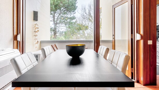A dining table with a black bowl centerpiece, white chairs, and a view of trees through a window. - Apartment 'Torralta' with Sea View, Wi-Fi and Air Conditioning (Carvalhal)