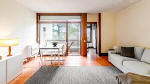 A modern living room with a sofa, a dining table with chairs, a lamp, and a large window. - Apartment 'Torralta' with Sea View, Wi-Fi and Air Conditioning (Carvalhal)