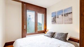 A bedroom with a large bed, a window with wooden frames, and three beach-themed wall art pieces. - Apartment 'Torralta' with Sea View, Wi-Fi and Air Conditioning (Carvalhal)