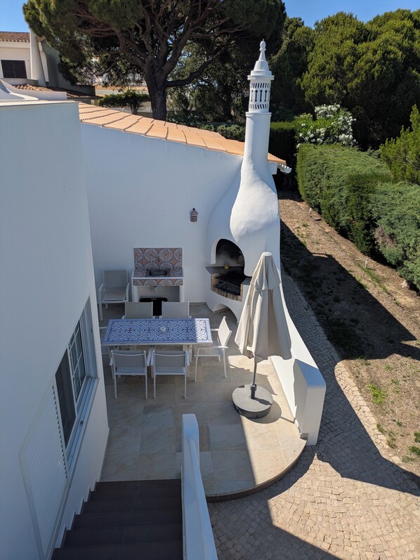Eine Terrasse mit Tisch und Stühlen, ein kleiner Kamin und ein weißes, turmartiges Gebäude.