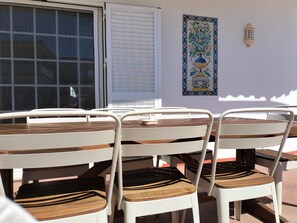 Un patio con mesa de madera y sillas de metal blanco.