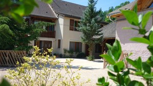 A two-story building with a balcony, a covered porch, and a gravel driveway. - Gîte des Cèdres - Ameugny (AMEUGNY)