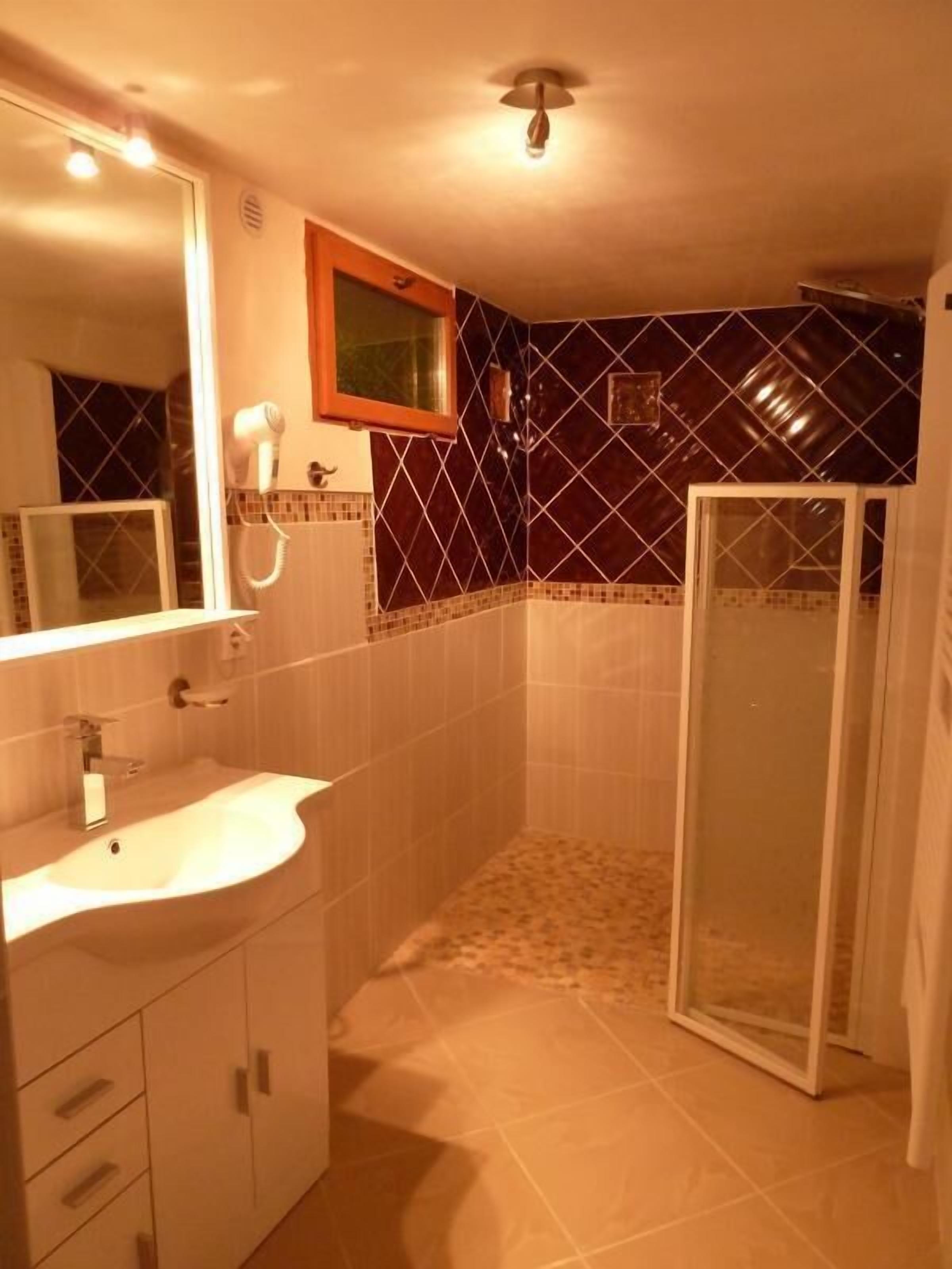 A bathroom with a sink, mirror, hairdryer, and a shower area.