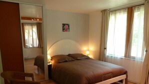 A bedroom with a bed, bedside table, lamp, chair, and a window with curtains. - Gîte des Cèdres - Ameugny (AMEUGNY)