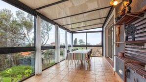 Une terrasse couverte avec une table et des chaises, de grandes fenêtres et une vue sur les arbres et les bâtiments.