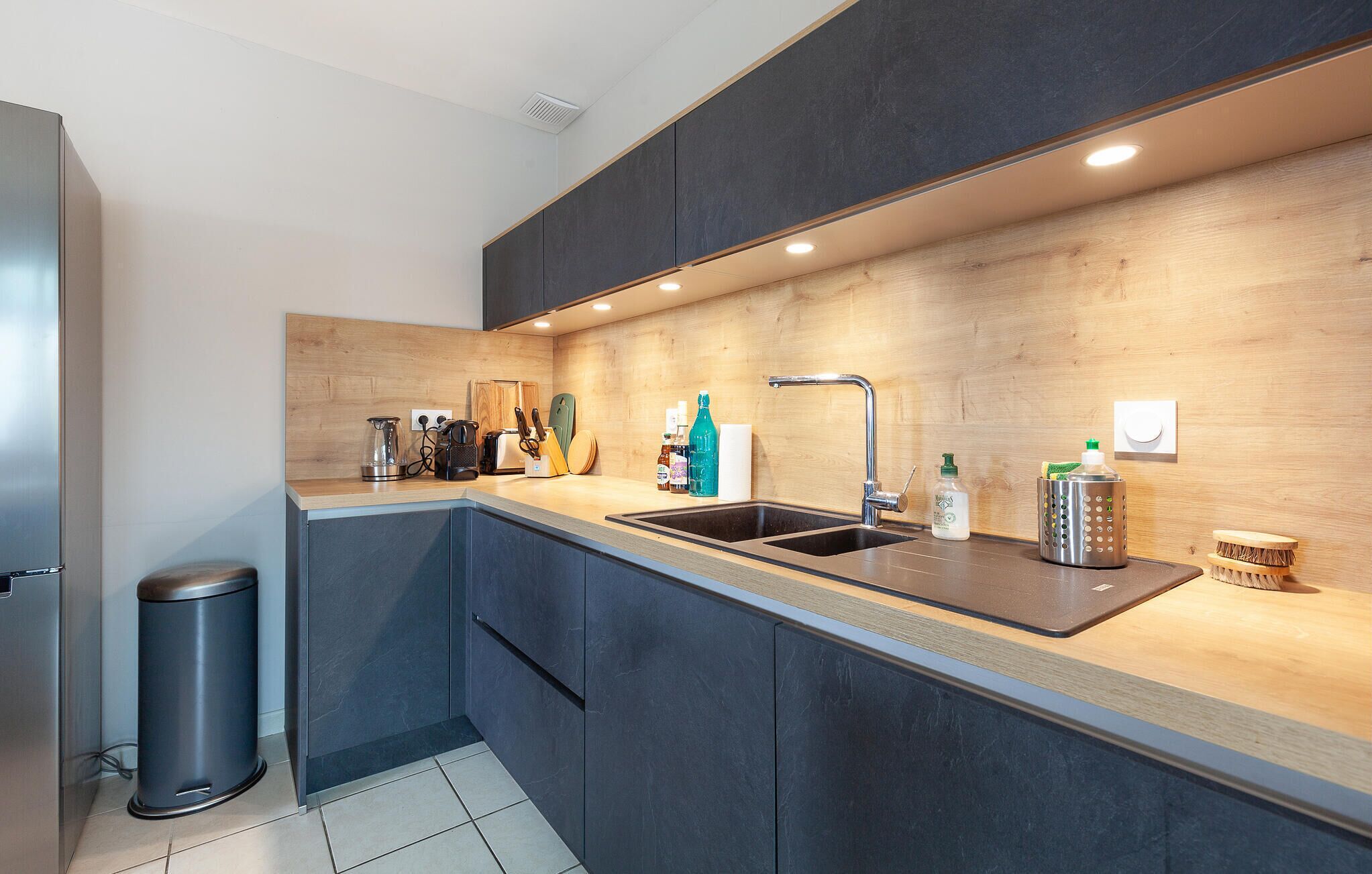 A modern kitchen with dark cabinets, a wooden countertop, and a stainless steel sink.