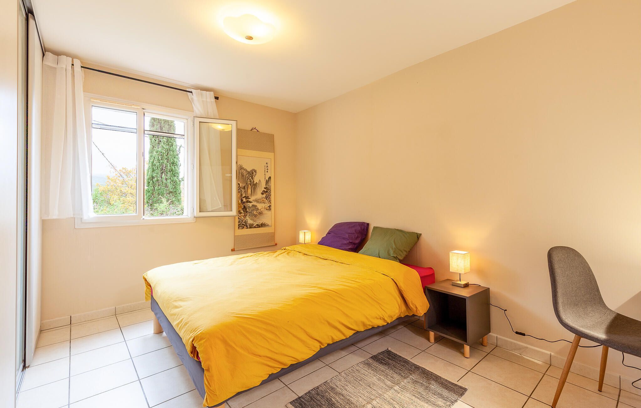 A bedroom with a bed, a chair, a nightstand, and a window with curtains.
