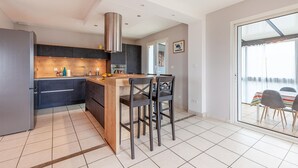 Une cuisine moderne avec des meubles de couleur sombre, un îlot central en bois et une grande fenêtre.