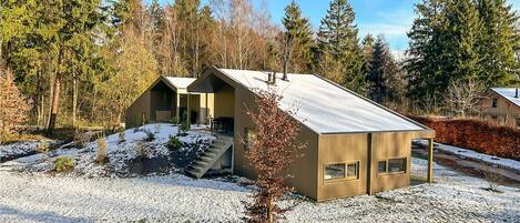A modern cabin with a sloped roof, a small porch, and a gravel driveway.