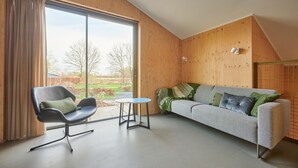Una sala de estar moderna con un amplio ventanal corredera, un sillón negro, un sofá gris y una pequeña mesa redonda.