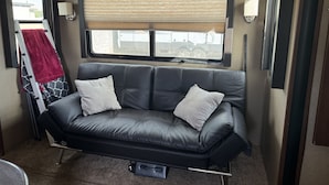 En svart lädersoffa med två kuddar, ett fönster med persienner och en röd handduk hängd på en stege.