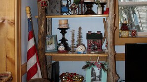 A cozy living room with a wooden shelf displaying holiday decorations, a television, and a comfortable couch. - Welcome to The Driftwood Cottage! A cozy 2-bedroom home in Grand Marais, MI. (Grand Marais)