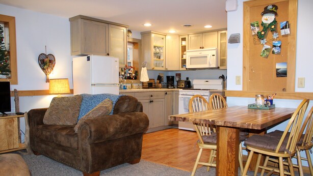 A cozy living room with a brown sofa, a wooden dining table, and a kitchen area with wooden cabinets and a microwave. - Welcome to The Driftwood Cottage! A cozy 2-bedroom home in Grand Marais, MI. (Grand Marais)