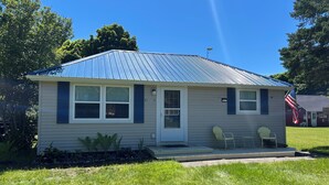 A single-story house with a metal roof, a front door, and two windows. - Welcome to The Driftwood Cottage! A cozy 2-bedroom home in Grand Marais, MI. (Grand Marais)