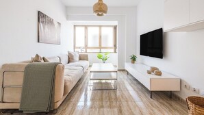 Ein modernes Wohnzimmer mit einer Couch, einem Couchtisch, einem an der Wand montierten Fernseher und einem großen Fenster.