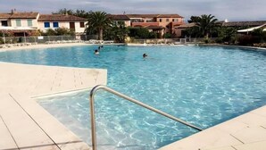 A swimming pool with clear blue water, surrounded by buildings and palm trees. - Villa la Provençale - Roquebrune SUR Argens (ROQUEBRUNE SUR ARGENS)